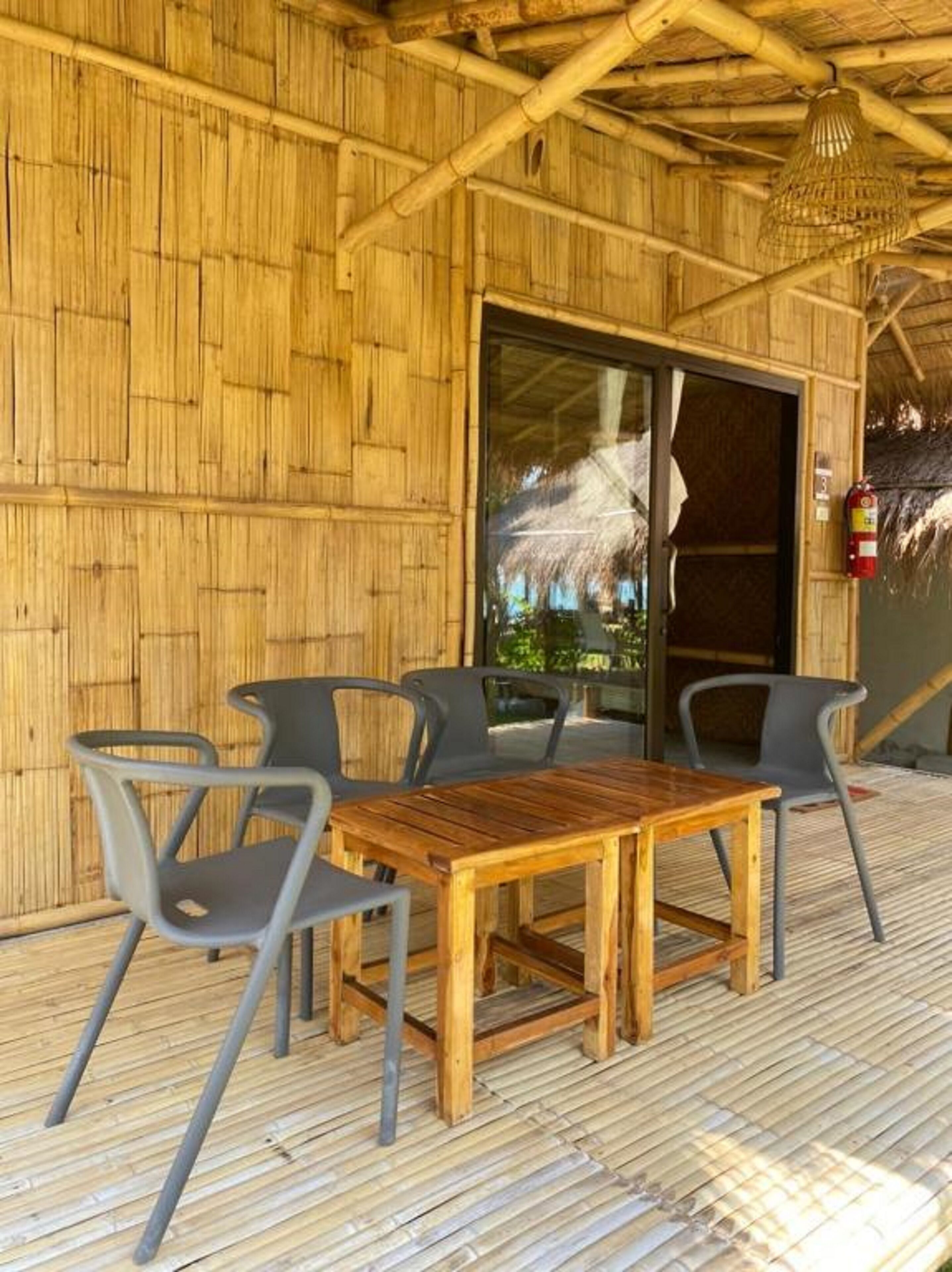 Un área de estar al aire libre con una mesa y sillas de madera, una puerta de cristal que da al interior y una pared de bambú.