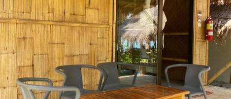 Un área de estar al aire libre con una mesa y sillas de madera, una puerta de cristal que da al interior y una pared de bambú.