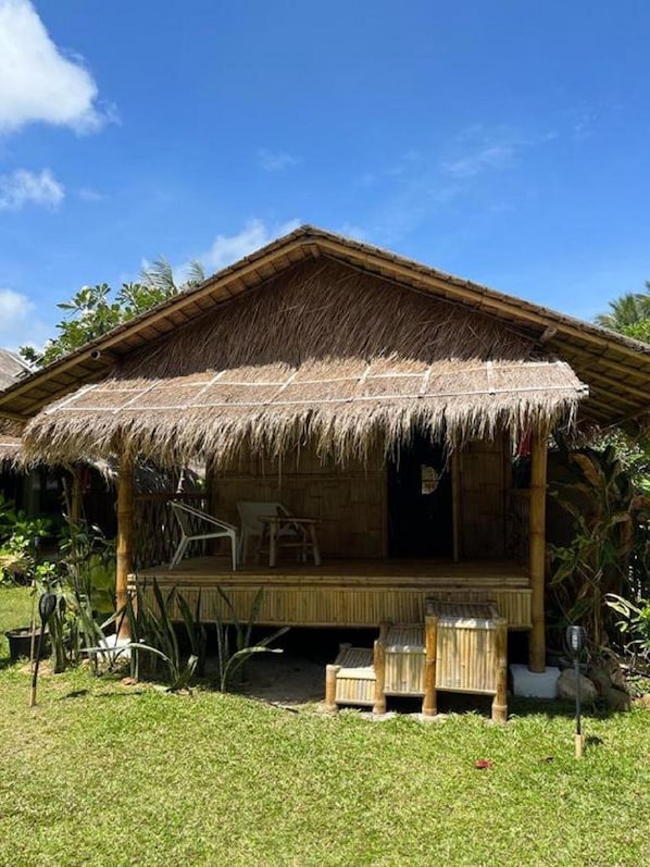 Una cabaña con techo de paja y un porche, rodeada de vegetación tropical.