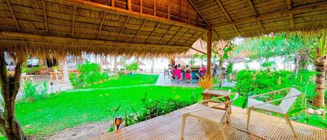 A covered outdoor area with a thatched roof, bamboo flooring, and seating arrangements.