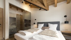Een moderne slaapkamer met een tweepersoonsbed, een douchecabine van glas, houten balken en uitzicht op de bergen.