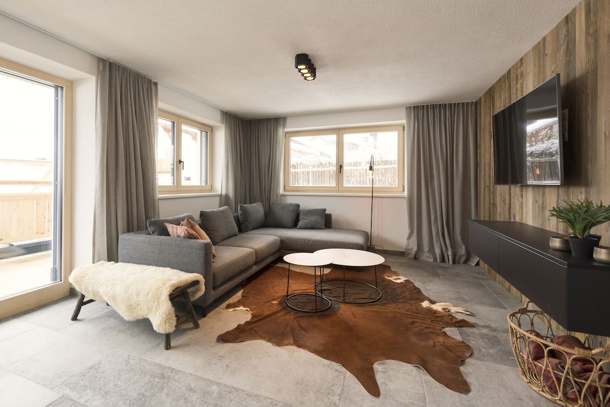 Ein modernes Wohnzimmer mit einem grauen Sofa, einem weißen Couchtisch und einem großen, braunen Lederteppich.
