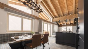 Een moderne keuken met een houten plafond, grote ramen en een eethoek met een tafel en stoelen.