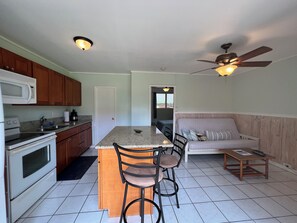 A compact kitchen with a central island, wooden cabinets, a microwave, and a ceiling fan.