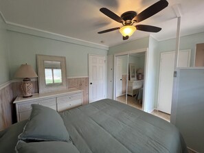 A bedroom with a bed, a ceiling fan, a dresser, a mirror, and a door leading to another room.