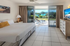 A hotel room with a bed, a TV, a desk with a lamp, and a balcony with a view of the sea. - Lagoon Lodge 003, Lagoon Lodge 003 on Hamilton Island (Hamilton Island)