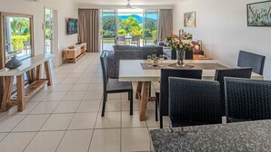 A spacious dining area with a large table, black wicker chairs, and a view of lush greenery and mountains through large windows.