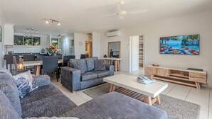 A modern living room with grey sofas, a white coffee table, and a painting of a beach scene.