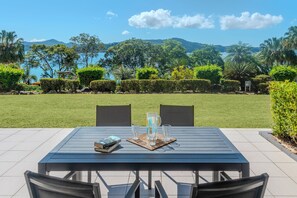 A patio table with chairs, a book, and a pitcher of water. - Lagoon Lodge 003, Lagoon Lodge 003 on Hamilton Island (Hamilton Island)