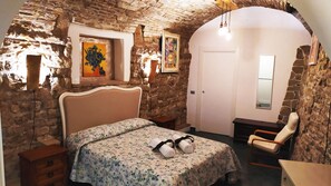 Ein Schlafzimmer mit Steinwand, einem Bett mit floralem Bettzeug, einem Sessel und Bildern an der Wand.