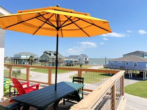A wooden deck with a table and chairs, a yellow umbrella, and a view of the beach and houses.
