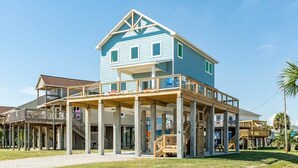 Une maison à deux étages située en bord de mer, dotée d’un balcon et d’une terrasse couverte.