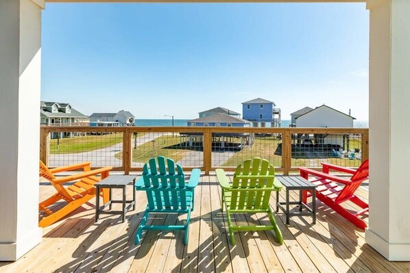 A balcony with colorful Adirondack chairs and a view of the beach and houses.