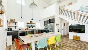 Une cuisine spacieuse équipée d’appareils modernes, un coin repas avec des chaises aux couleurs vives et un escalier menant à l’étage supérieur.