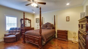 Un dormitorio con una cama con dosel, un aparador de madera, una mesita de noche, un sillón de cuero y un ventilador de techo.