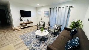 Una sala de estar con sofá, sillones, una mesa de centro, televisor y planta.