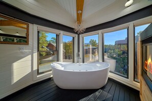 A modern bathroom with a freestanding bathtub, large windows, and a chandelier.