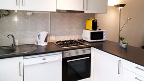A modern kitchen with white cabinets, a gas stove, a microwave, and a kettle. - Casa da Travessa (Horta)