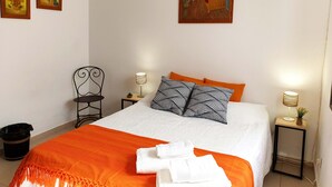 A neatly arranged bedroom with a bed, two bedside tables, a chair, and three paintings on the wall. - Casa da Travessa (Horta)