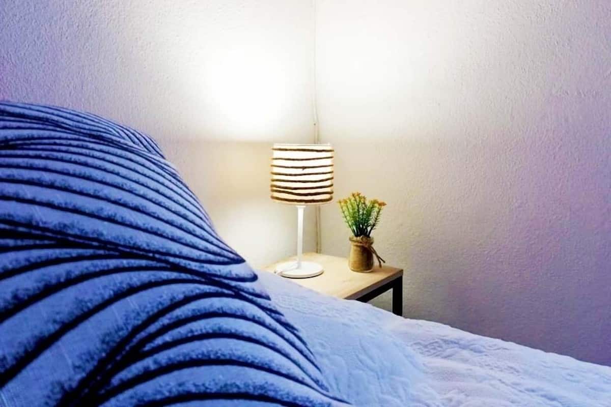 A bed with a blue striped blanket, a bedside table with a lamp and a small plant.