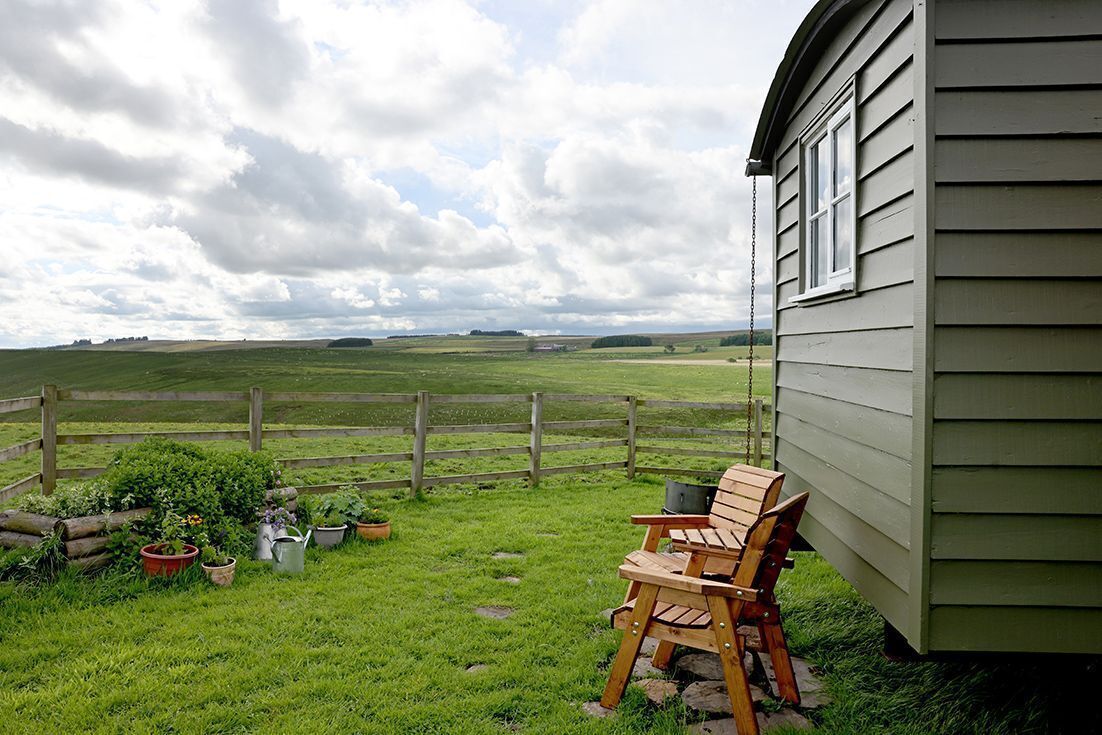 A wooden chair outside a house with a view of a grassy field.