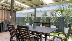Eine Terrasse im Freien mit Holztisch und -stühlen, einem Grill und Kübelbäumen.