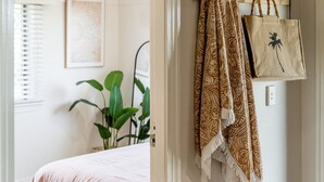 Ein Schlafzimmer mit einem Bett, einer Pflanze und einer Tür mit einem gemusterten Vorhang und einer Stofftasche.