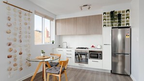 A modern kitchen with a dining area, featuring a glass table, wooden chairs, a stainless steel refrigerator, and a built-in oven. - Cocomo Stylish Pet Friendly Elwood Apartment (Elwood)