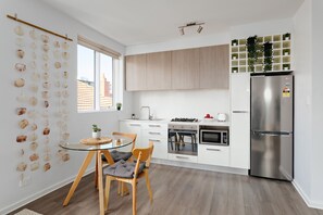 A modern kitchen with a dining area, featuring a glass table, wooden chairs, a stainless steel refrigerator, and a built-in oven. - Cocomo Stylish Pet Friendly Elwood Apartment (Elwood)