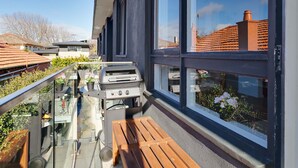 Un balcon doté d’un barbecue, d’un banc en bois et d’une rambarde en verre donnant sur un quartier résidentiel.