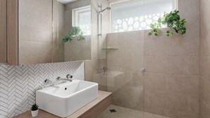 Une salle de bain moderne avec un lavabo rectangulaire, une douche en verre et un mur orné d’un motif en chevrons.