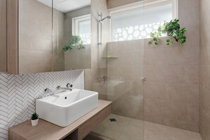 A modern bathroom with a rectangular sink, a glass shower enclosure, and a herringbone-patterned wall. - Cocomo Stylish Pet Friendly Elwood Apartment (Elwood)