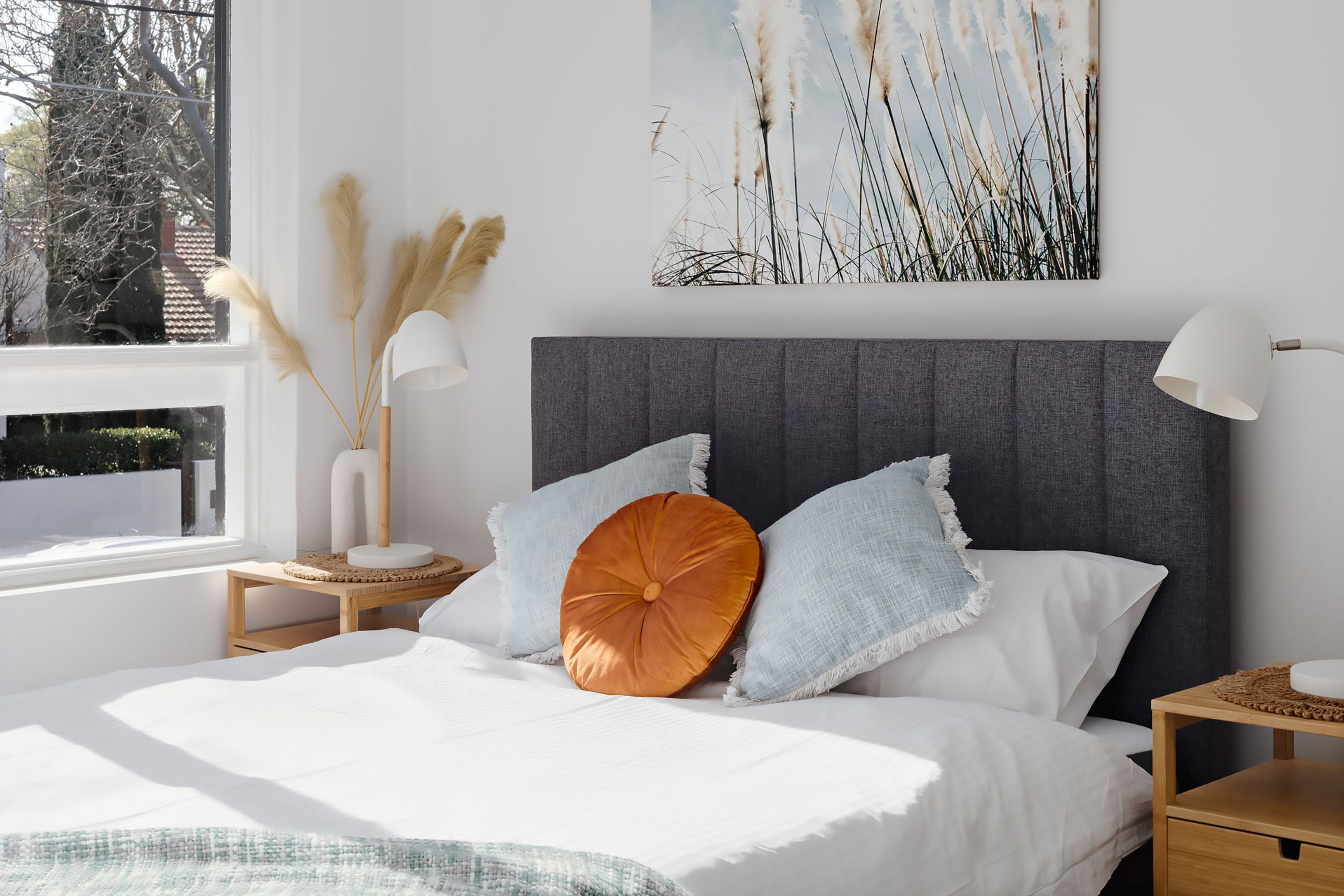 Une chambre à coucher avec un lit, une table de chevet, une lampe et une fenêtre donnant sur des arbres.