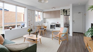 A modern apartment with a dining area, kitchen, and living room. There is a large window providing natural light and a view of the outside. - Cocomo Stylish Pet Friendly Elwood Apartment (Elwood)