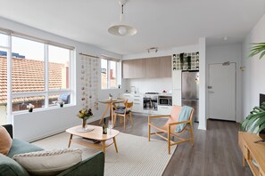 A modern apartment with a dining area, kitchen, and living room. There is a large window providing natural light and a view of the outside. - Cocomo Stylish Pet Friendly Elwood Apartment (Elwood)