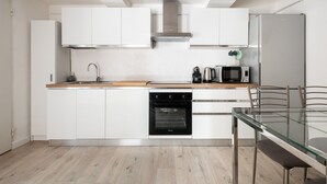 Une cuisine moderne avec des meubles blancs, un four en acier inoxydable, un micro-ondes et une table à manger en verre.