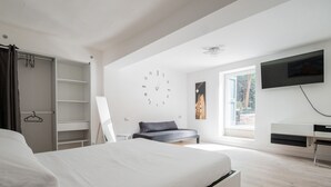 Une chambre moderne comprenant un lit, une armoire, un bureau, une télévision et une grande fenêtre.