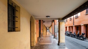 Un couloir bordé d’une rangée de motos garées sur le côté droit, menant à un bâtiment à la façade jaune et au sol carrelé.