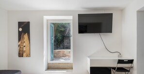 A modern room with a bed, a desk with a chair, a TV, and a painting.