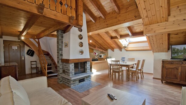 A cozy cabin interior with a stone fireplace, wooden beams, a dining area, and a TV. - Apartment Alpina (Zermatt)