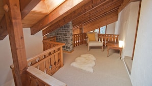 A cozy attic room with a stone fireplace, wooden furniture, and a white fur rug. - Apartment Alpina (Zermatt)