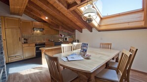 A cozy kitchen with wooden cabinets, a dining table with chairs, and a skylight above. - Apartment Alpina (Zermatt)