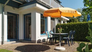 A patio with a table and chairs, an umbrella, and a hedge in the background. - Apartment for up to 4 people,central,quiet,south-facing terrace,sauna,WLAN,bicycle shed,parking lot (Prerow)