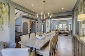 A spacious dining area with a long table, chairs, and a chandelier. There is a staircase leading to another level.