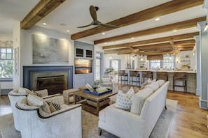 A spacious living room with a fireplace, a large sofa, and a dining area with a kitchen in the background.
