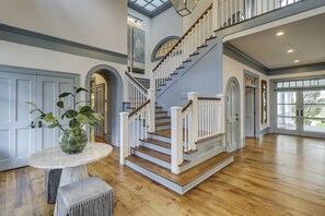 A spacious interior with a grand staircase, wooden flooring, and a large window offering a view of the outdoors.
