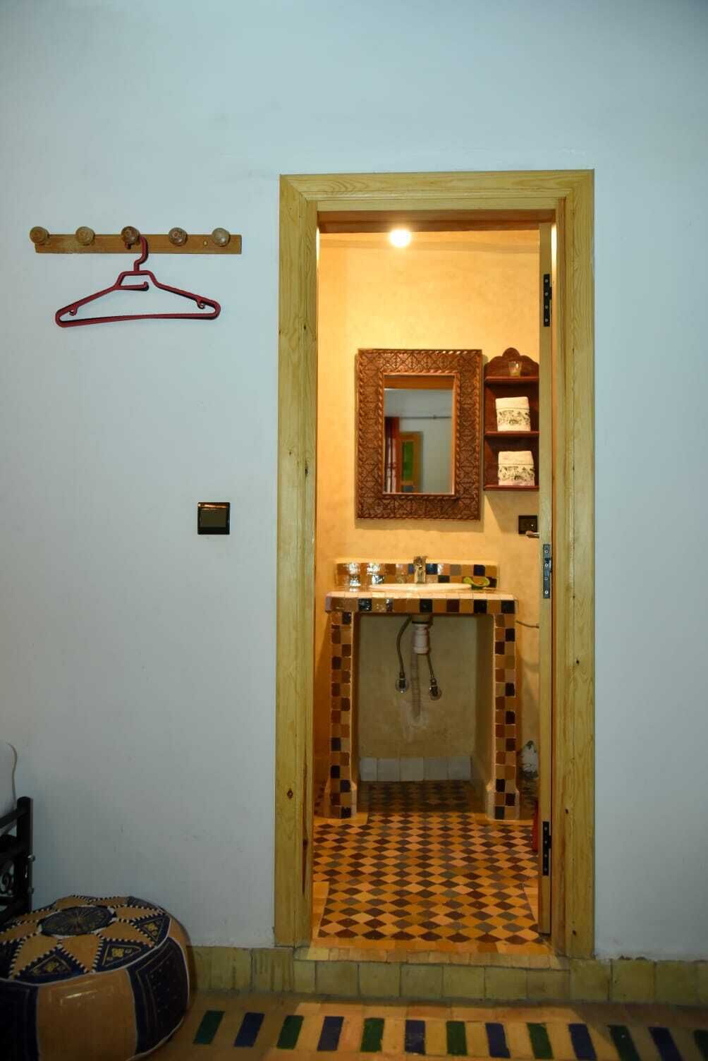 A bathroom with a wooden door, a mirror, a sink, and a hanging towel rack.