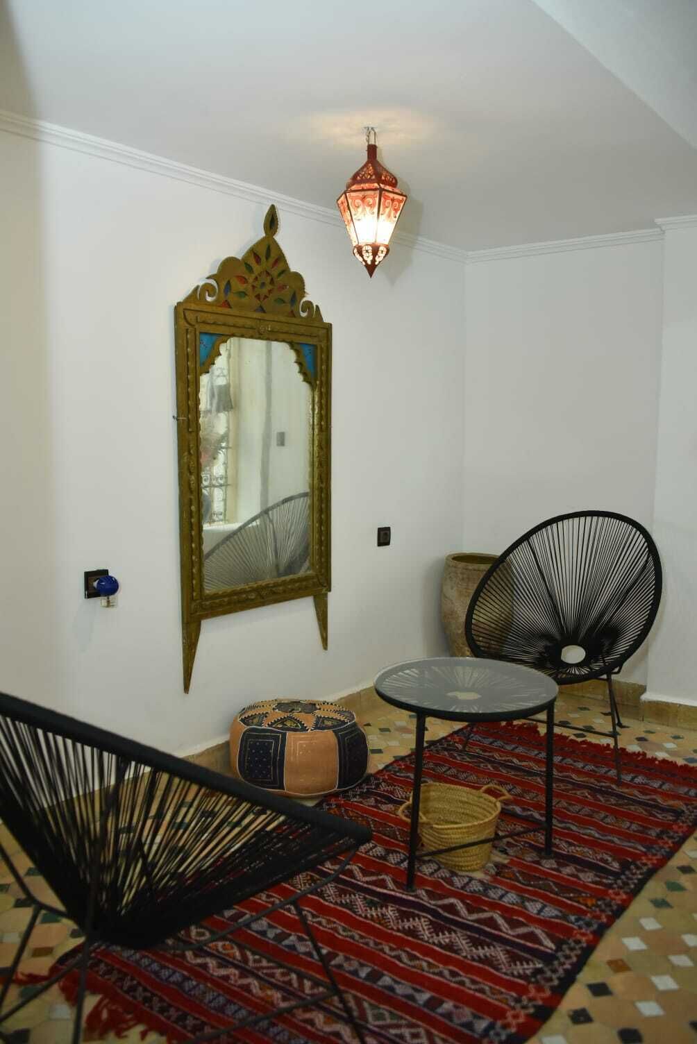 A room with a large ornate mirror, a black chair, a small round table, and a patterned rug.