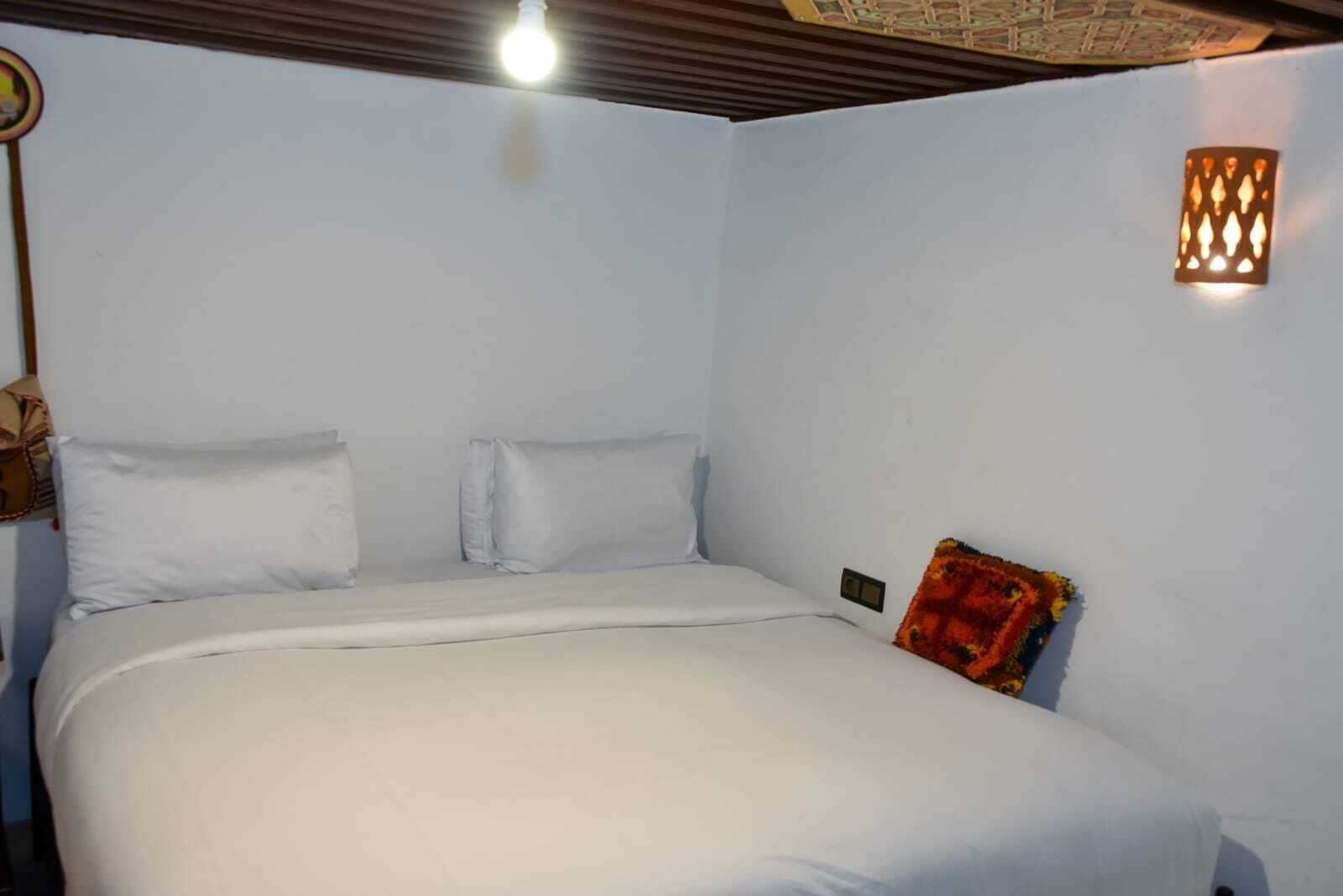 A neatly made bed with white linens in a room with white walls and a wooden ceiling.