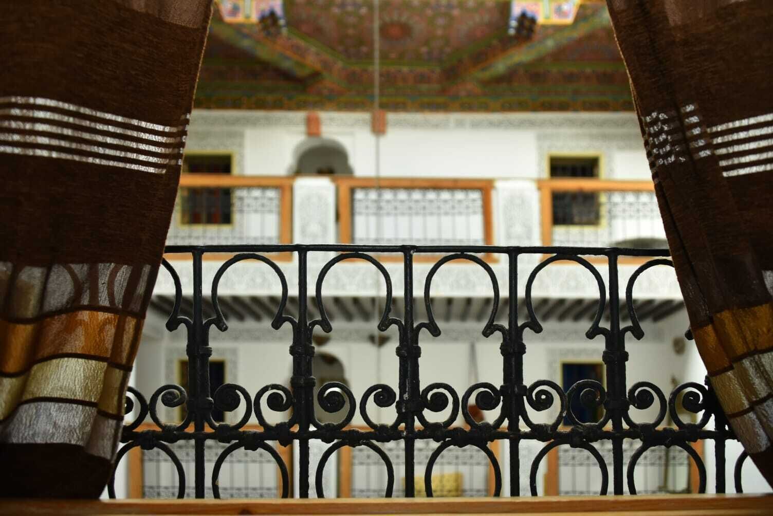 A view through ornate black wrought iron balcony railings with a patterned ceiling and architectural details in the background.